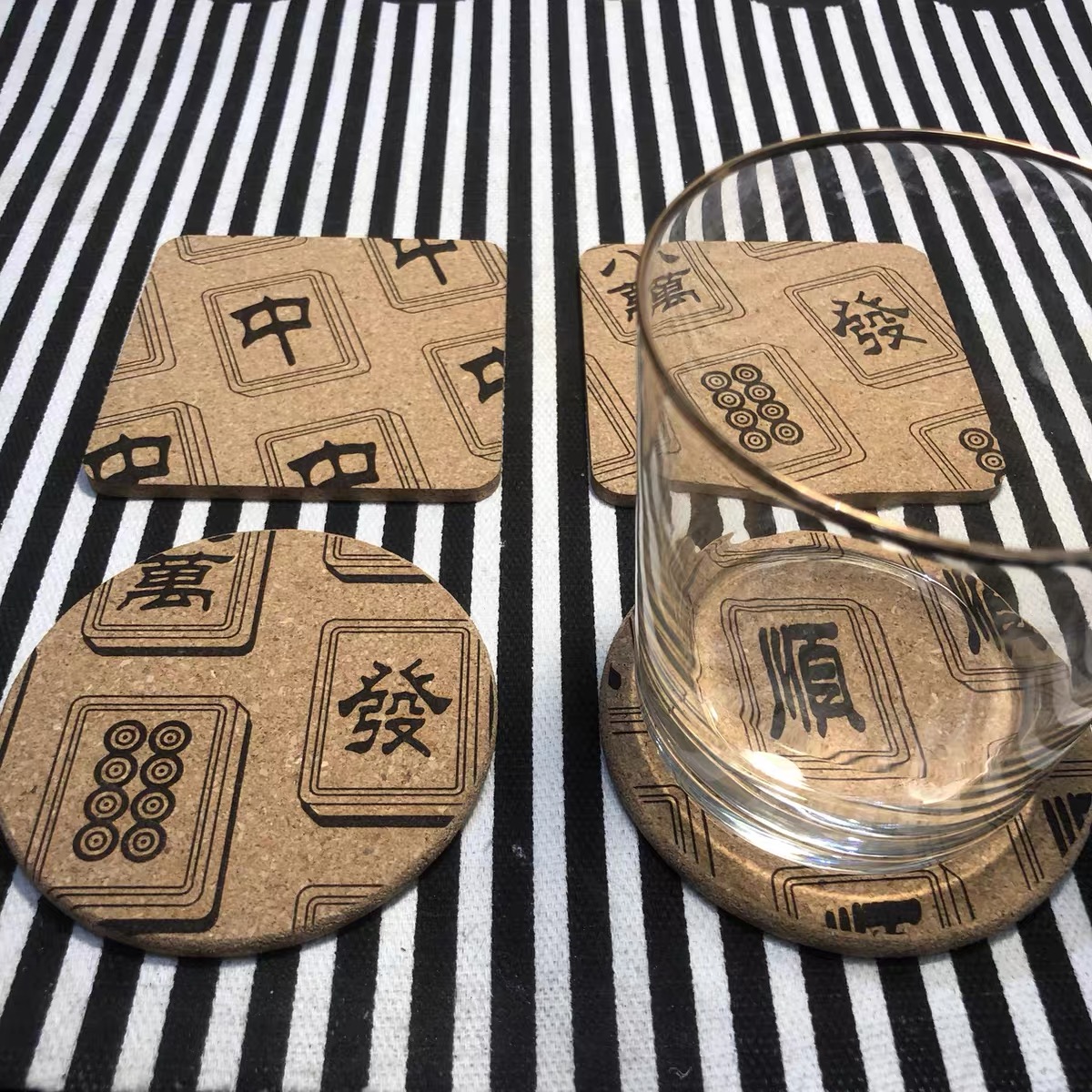 Cork coasters burnt with mahjong tile faces, one under a glass