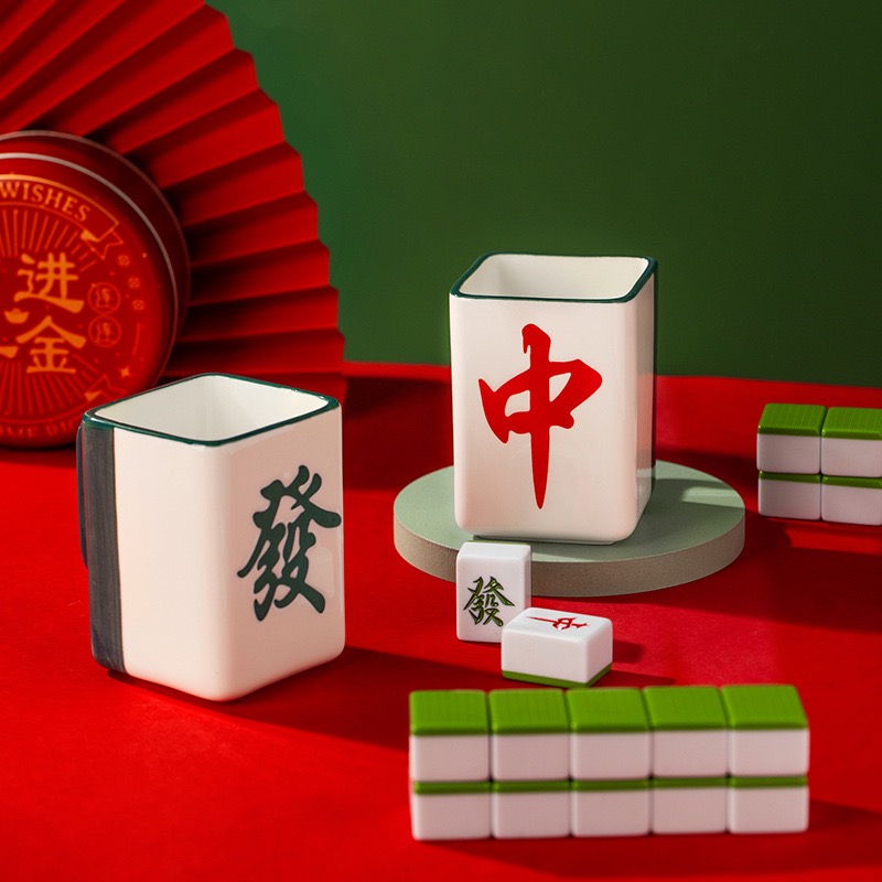 Two mahjong tile cups, zhong in red and fa in green, beside a stack of tiles